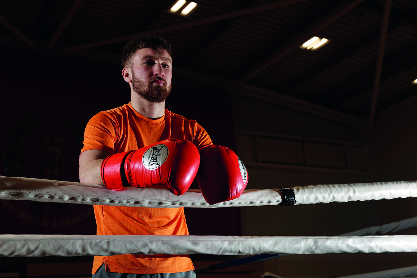 Boxer wearing gloves and leaning on boxing ring ropes