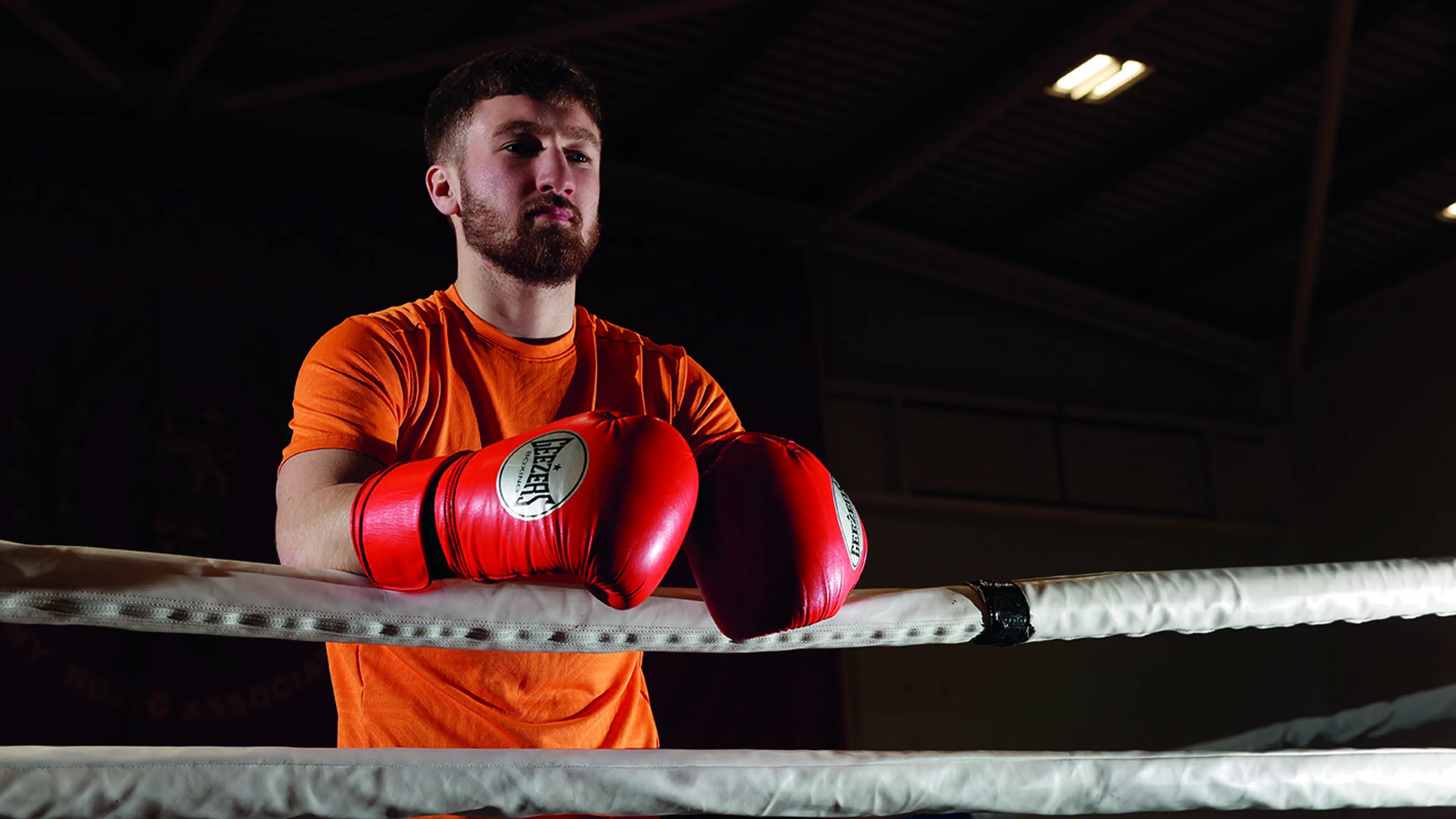 Boxer wearing gloves and leaning on boxing ring ropes