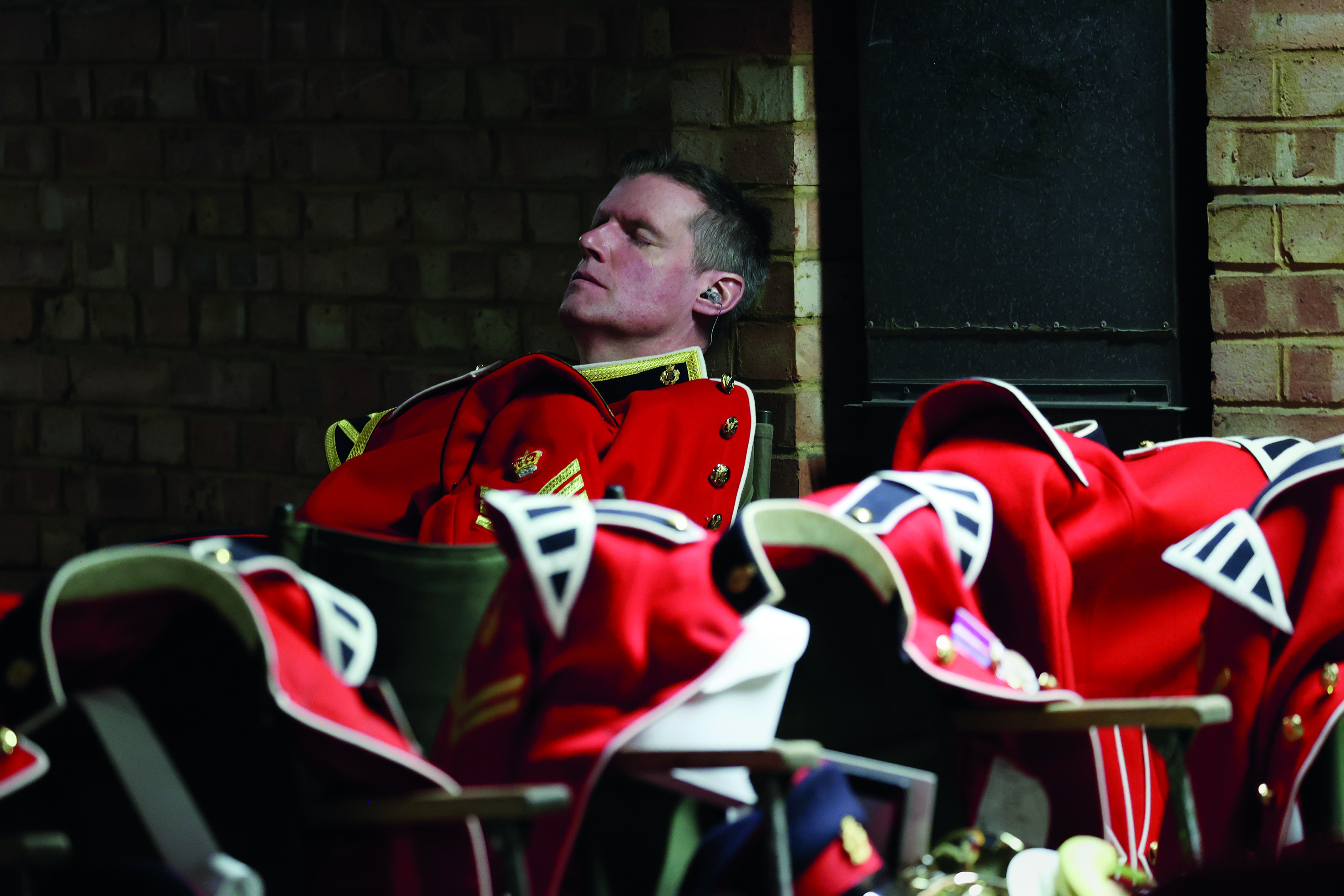 Soldier sleeping leaning against a brick wall wearing a red uniform