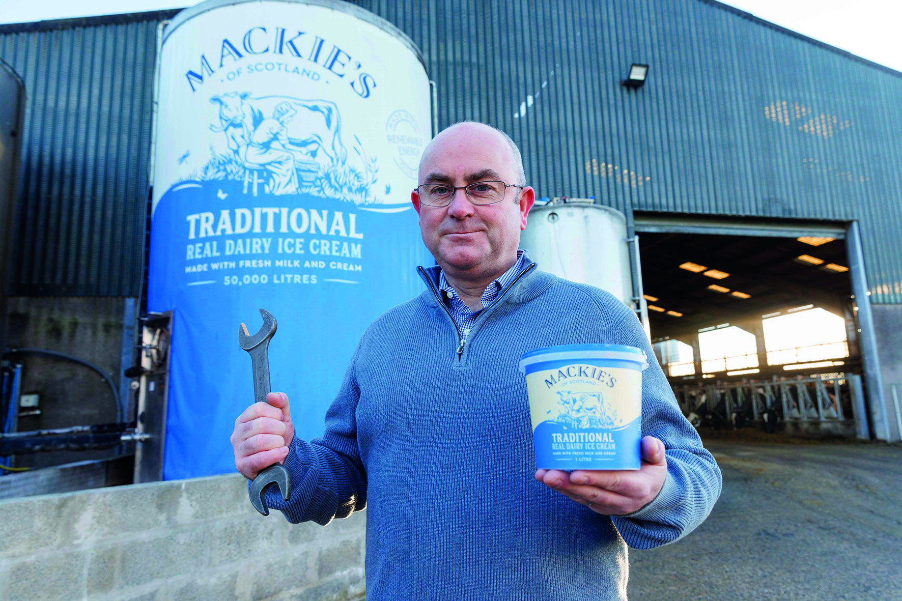 Man holding tub of ice cream in front of ice cream sign
