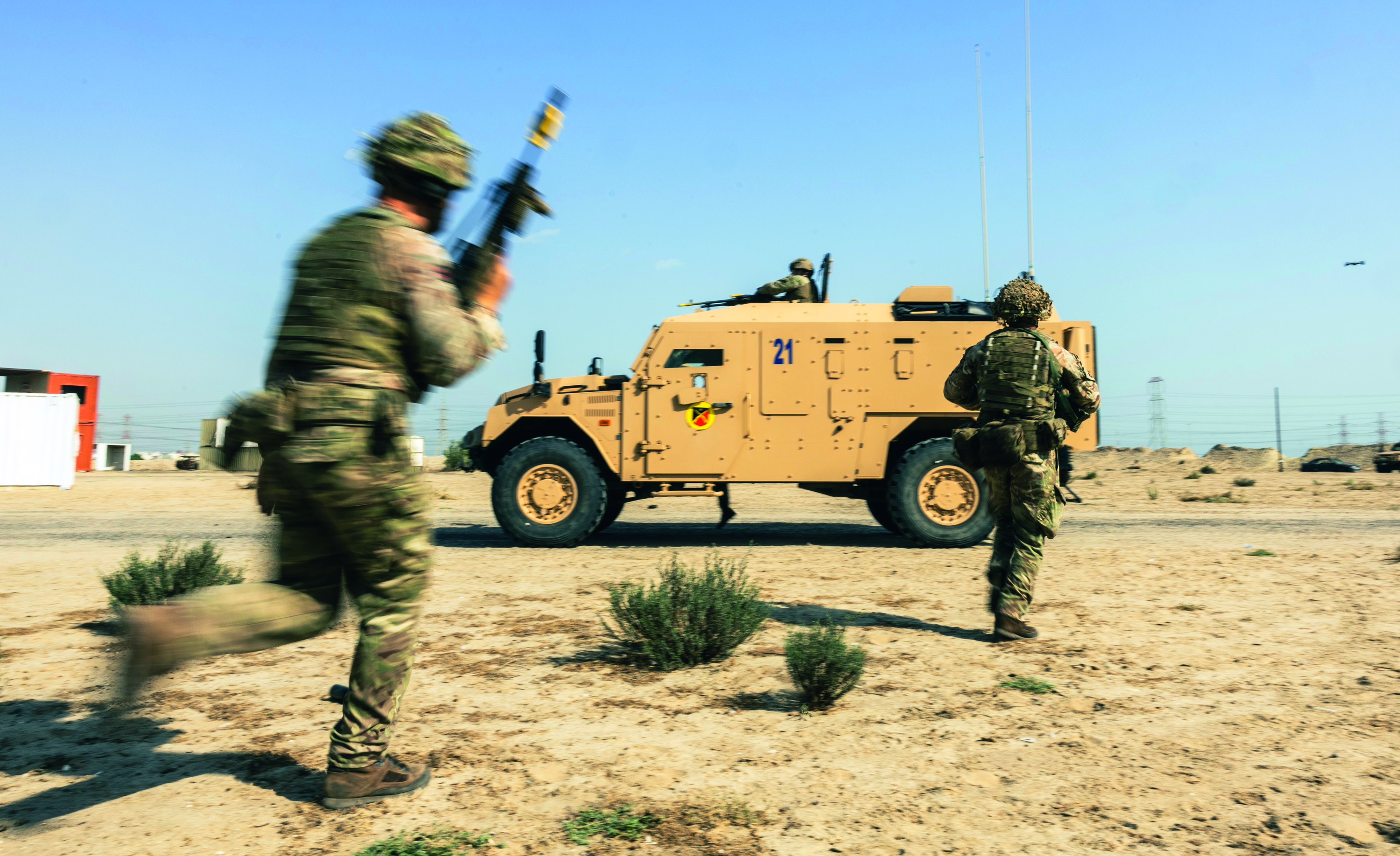 Two soldiers in desert, running towards military vehicle holding another soldier