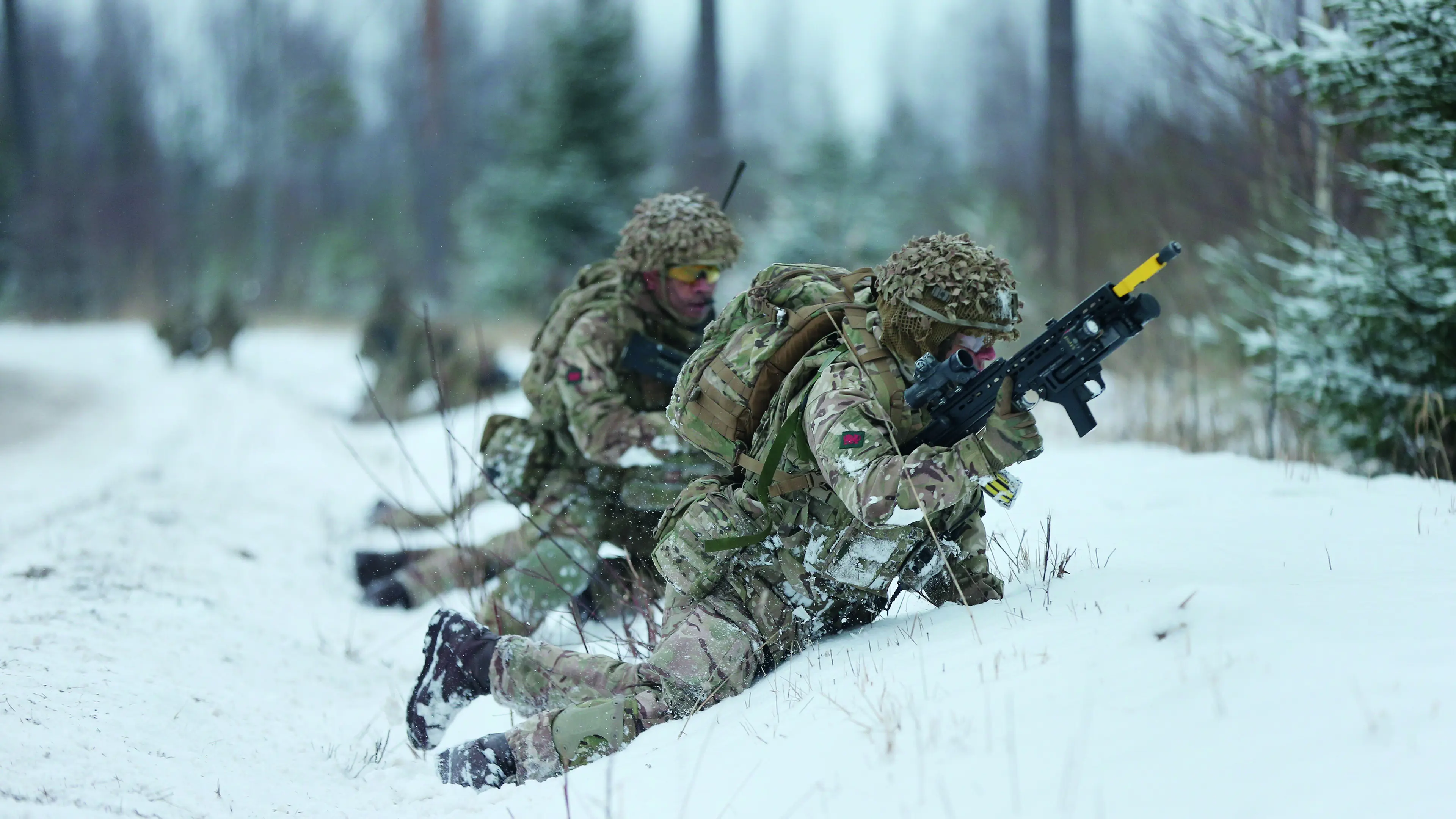 Two soldiers with guns crouching in the snow