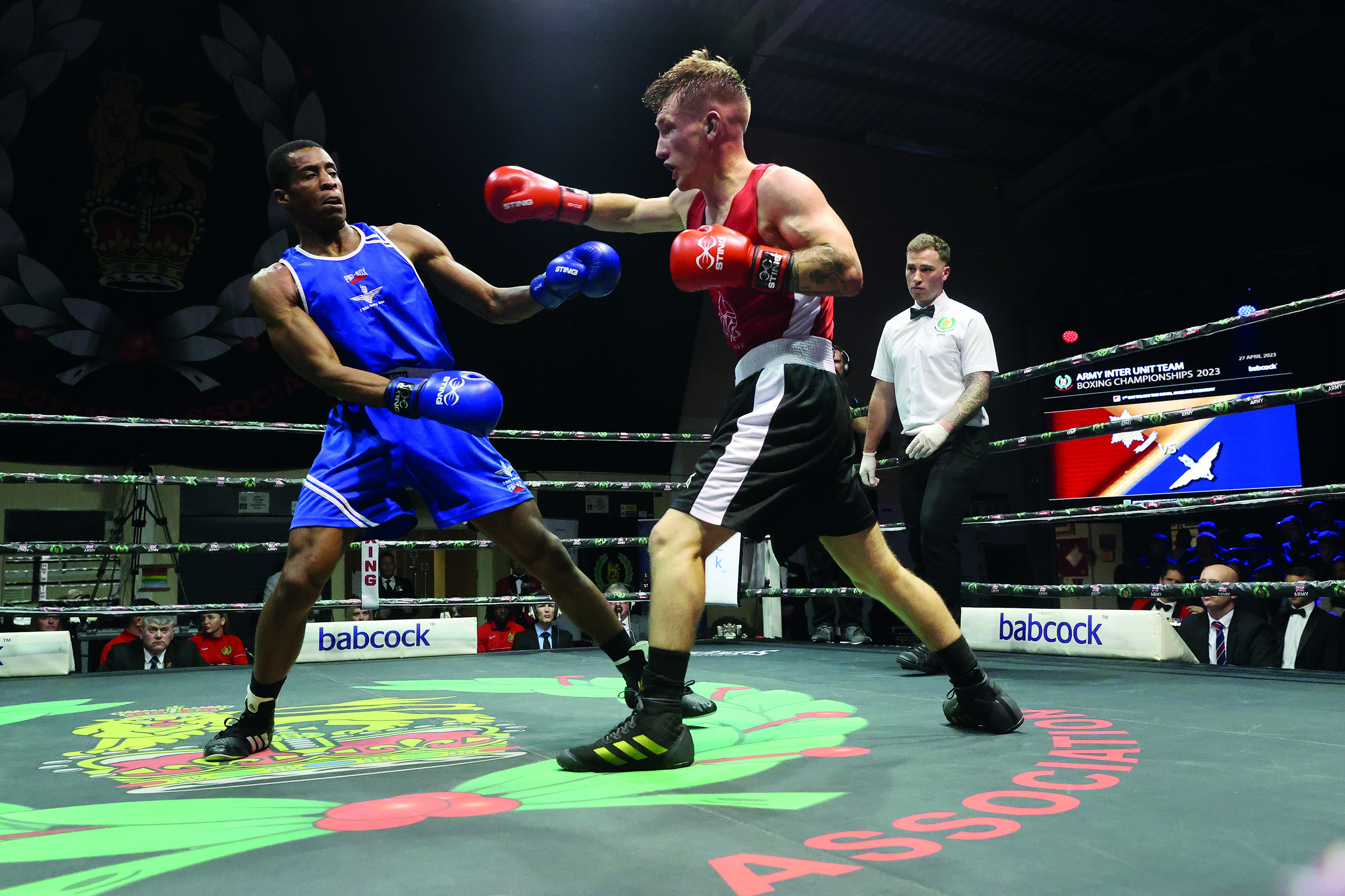 Two boxers fighting in the ring with referee in background