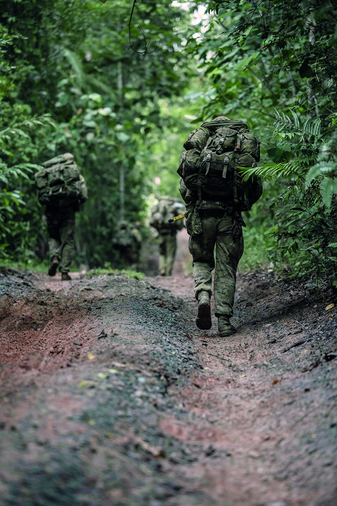 3 soldiers walking through wooded area along a muddy path
