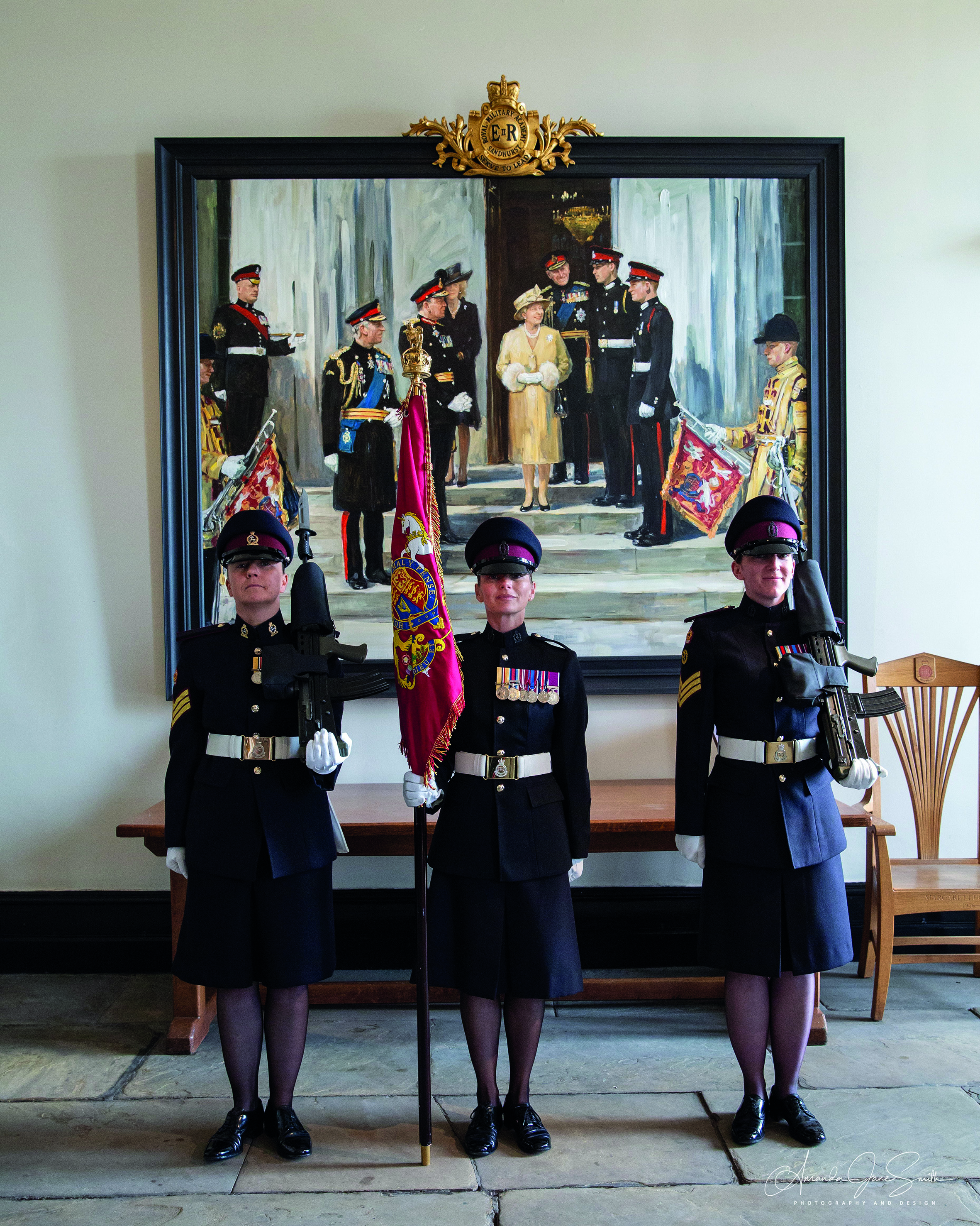 Three female soldiers standing in front of Queen portrait
