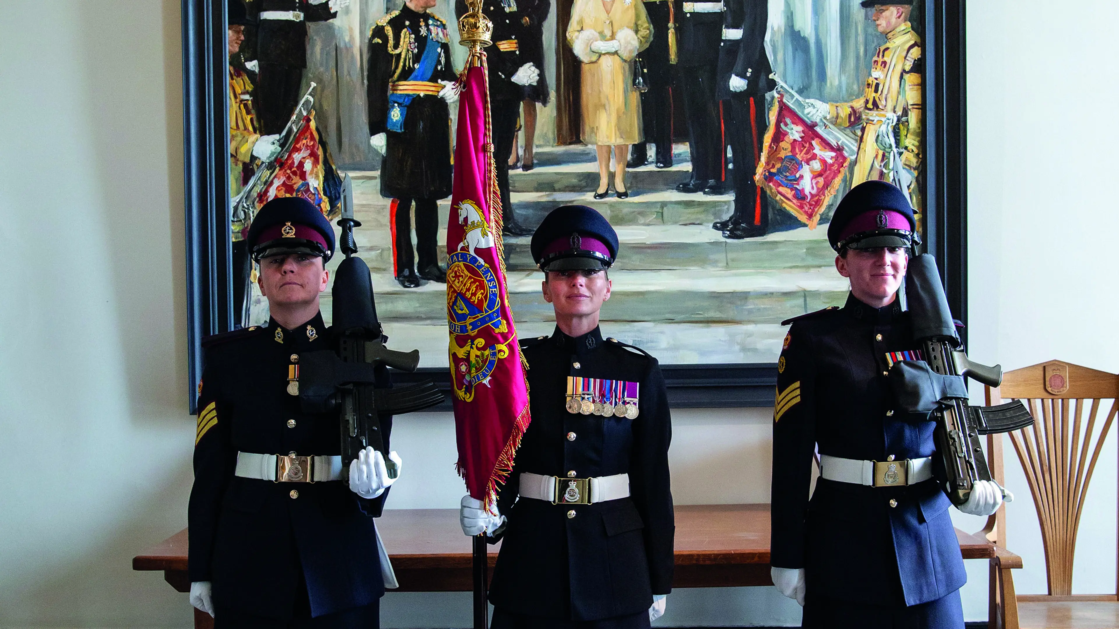Three female soldiers standing in front of Queen portrait