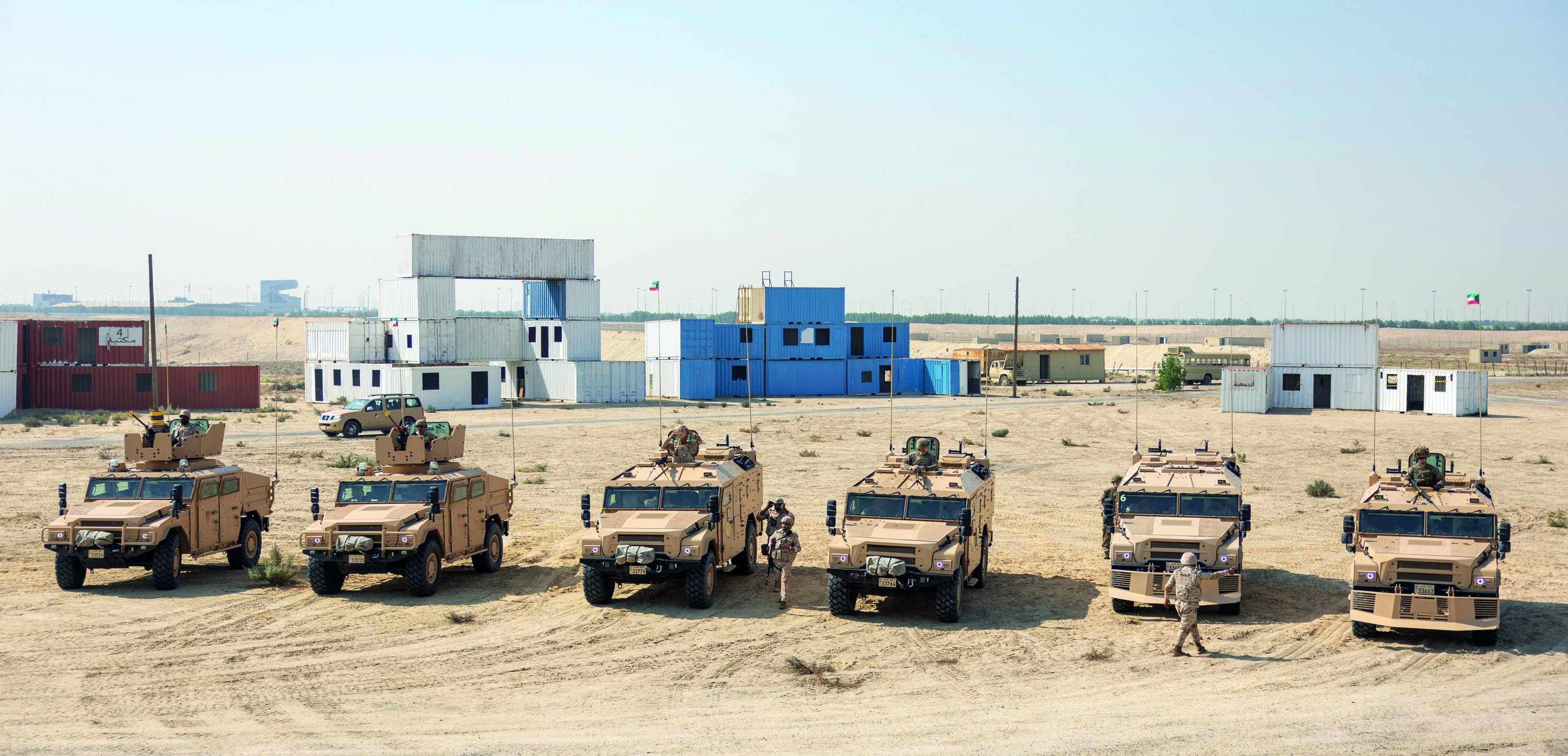 Six Army vehicles in desert with soldiers around