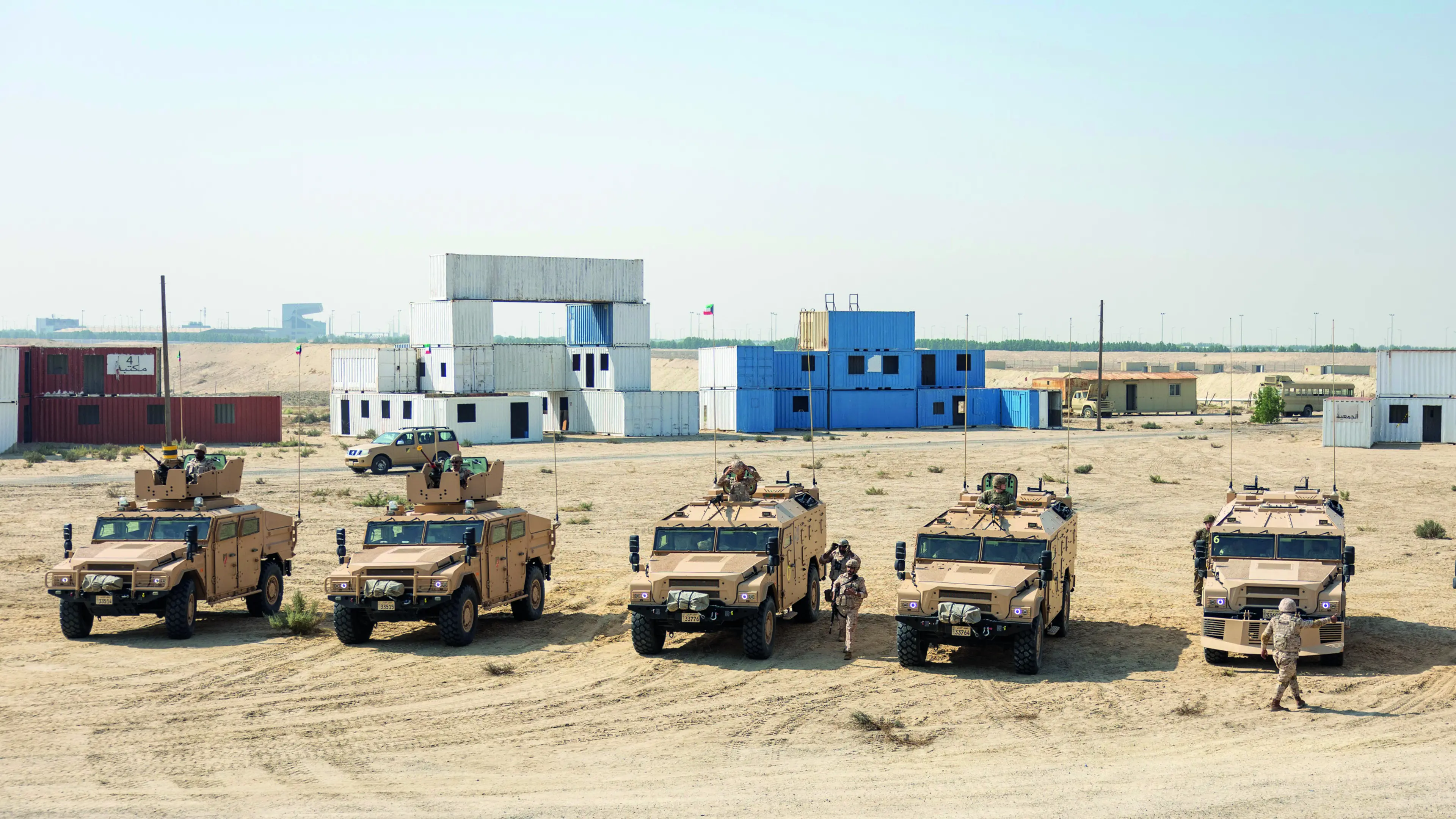 Six Army vehicles in desert with soldiers around