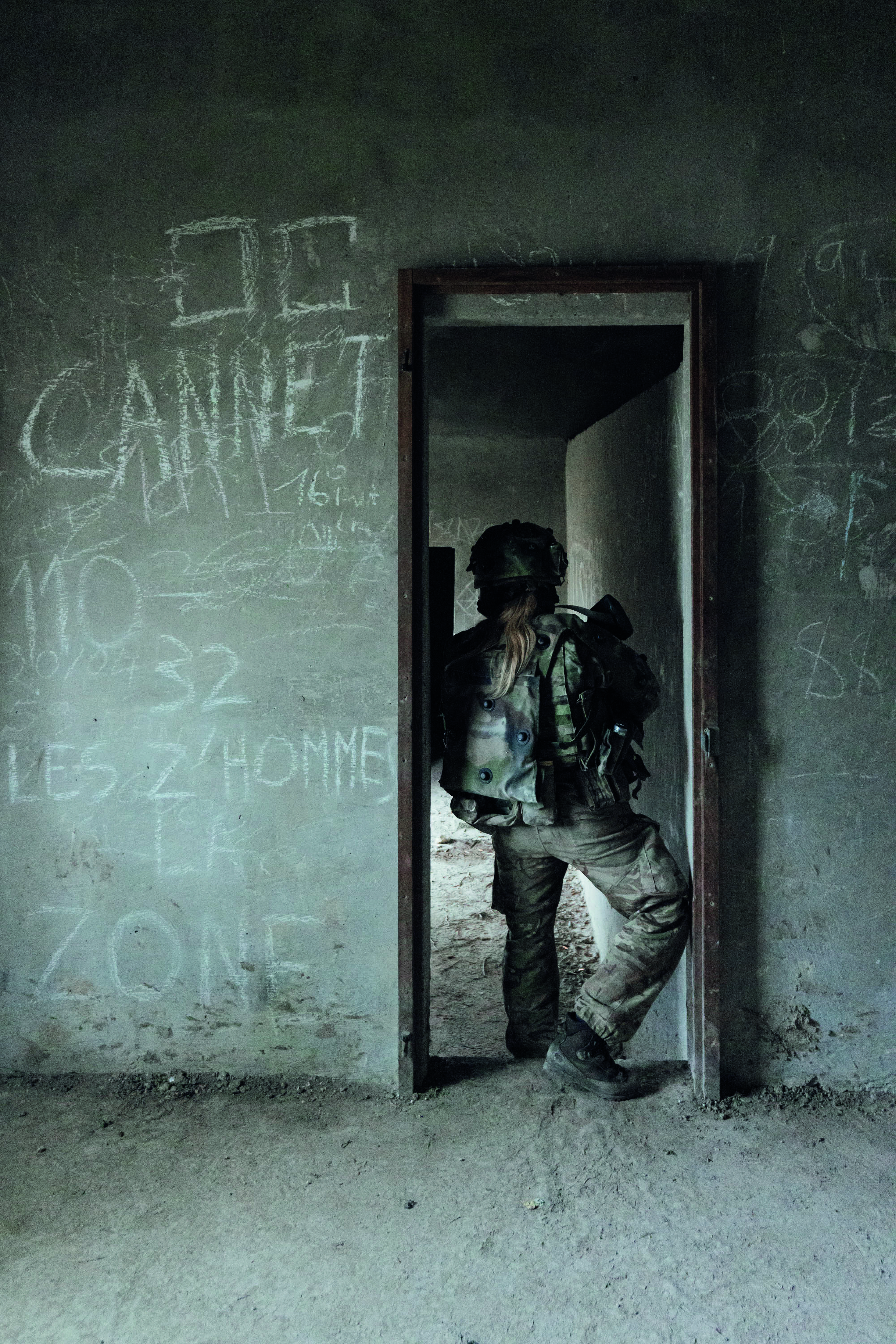 Female soldier standing in a doorway of an abandoned room filled with graffiti 