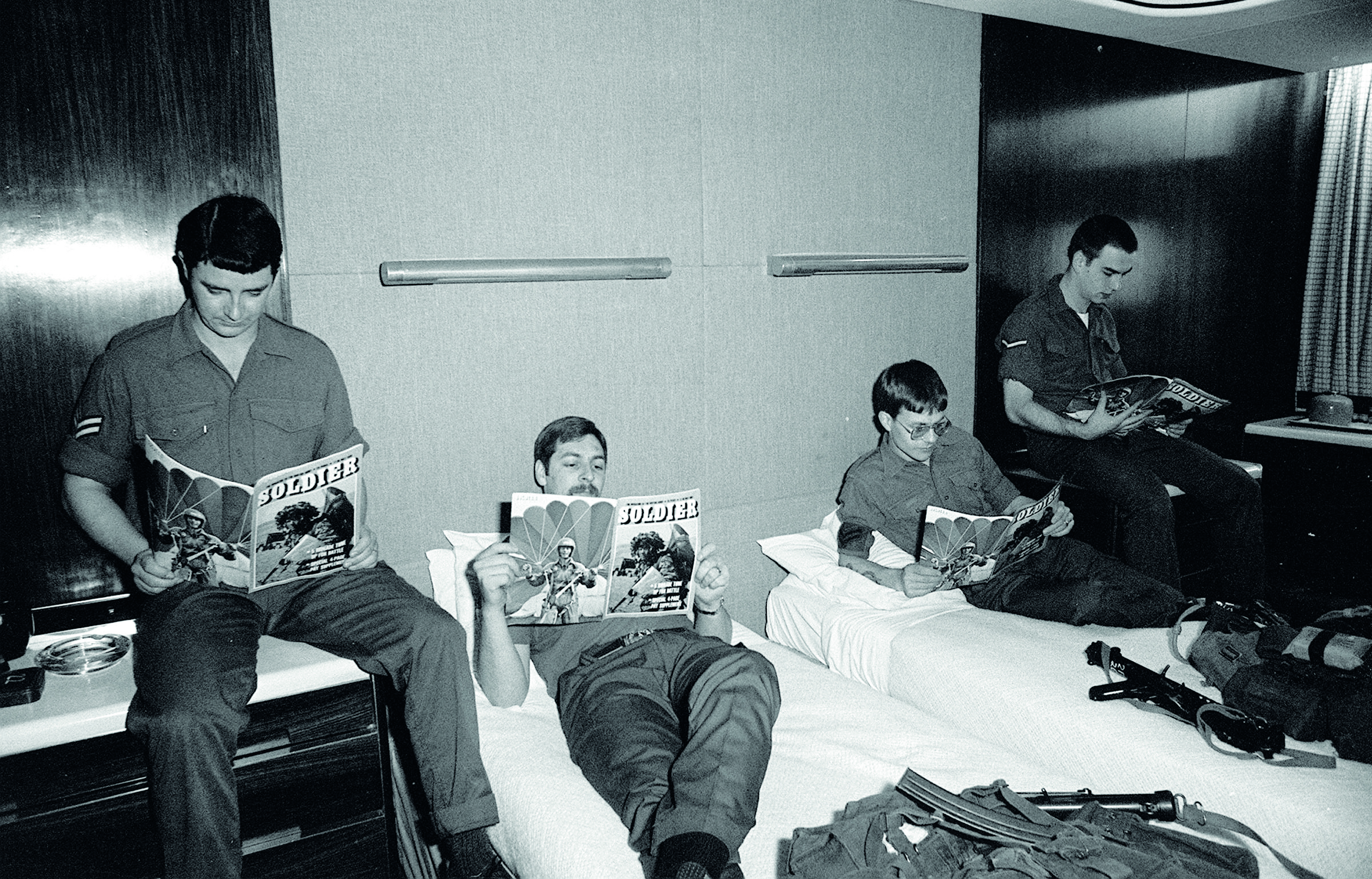 Black and white image of soldiers reading Soldier magazine in a hotel room