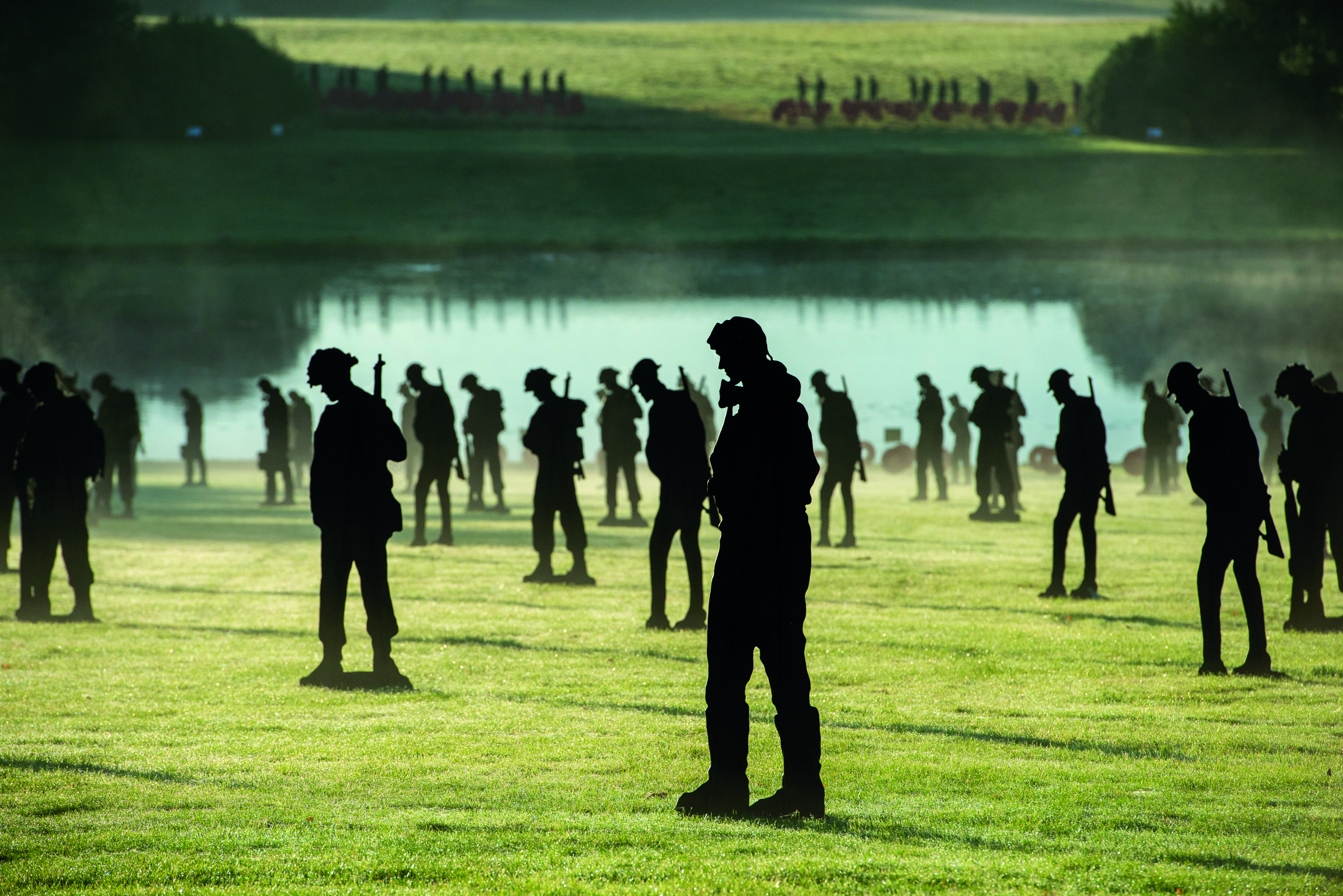 Silhouettes of multiple soldiers on grass with a lake behind them
