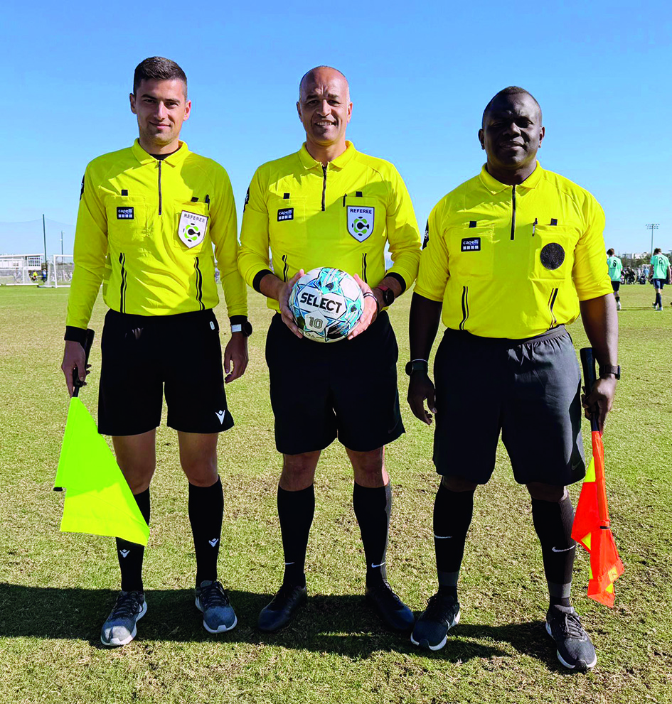 3 men in yellow football shirts smiling at the camera, 1 is holding a football