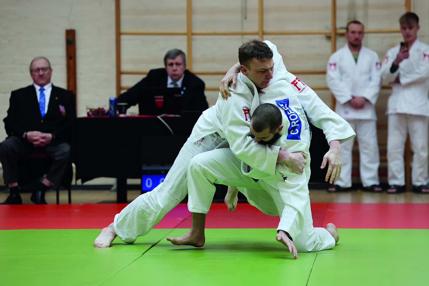 2 men practicing judo with onlookers and judges
