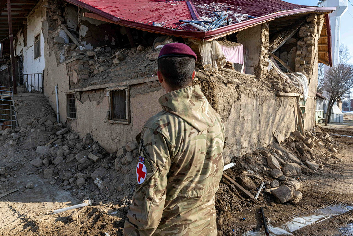 Military medic looking at damaged house